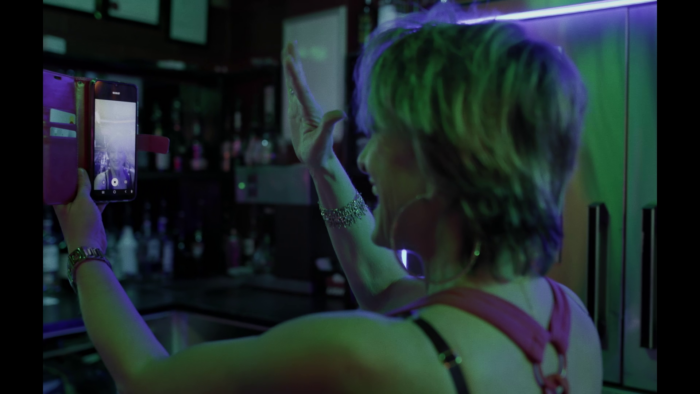 Une femme de profil, presque de dos, se regarde en souriant dans une exclamation de grande joie dans un téléphone.
